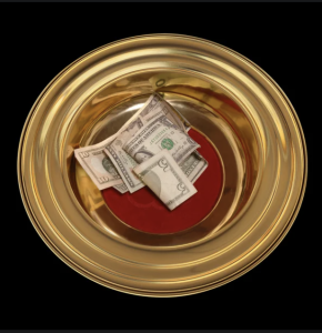 Brass offering plate with some cash in it, on a table with a dark cloth